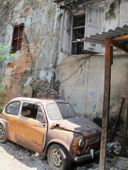 The old car wrecks in the alley with cracked walls