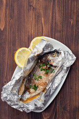 baked fish with lemon in aluminium foil on brown wooden background