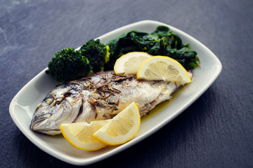 baked fish with lemon in white dish on ceramic background