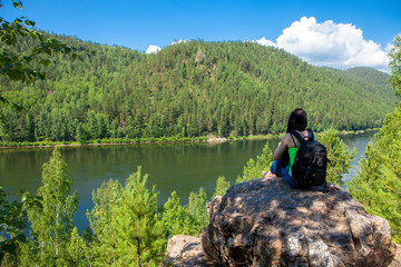 Young traveling woman sitting on the top of the mountain cliff.