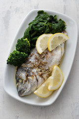 baked fish with lemon in white dish on ceramic background