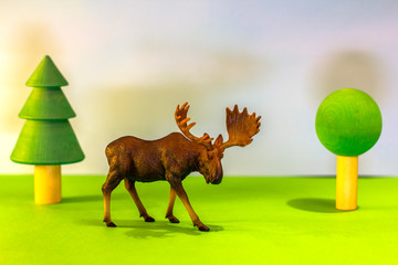 Toy elk in a toy forest. like a real moose on a bright studio background with wooden trees. Eco toys.