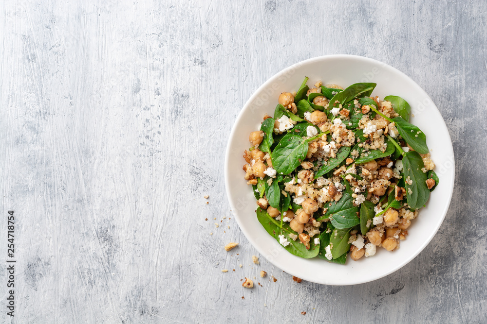 Wall mural Healthy salad with spinach, chickpeas, quinoa, feta cheese and walnuts in white plate on concrete background. Top view. Copy space. - Wall murals