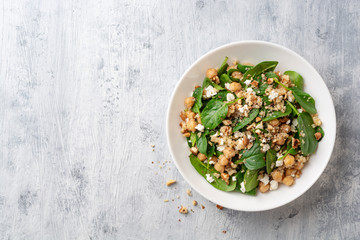 Healthy salad with spinach, chickpeas, quinoa, feta cheese and walnuts in white plate on concrete...