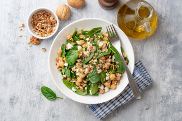 Healthy salad with spinach, chickpeas, quinoa, feta cheese and walnuts in white plate on concrete background. Top view.