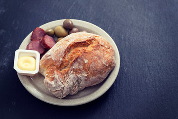 bread with butter, olives and smoked sausage on dish on ceramic background