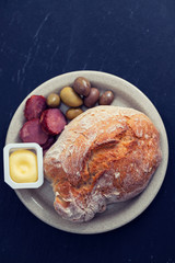 bread with butter, olives and smoked sausage on dish on ceramic background