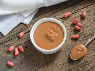 Peanut butter in a white bowl on a wooden table. Natural healthy nutrition and organic food