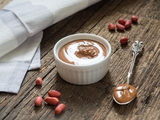 Peanut butter in a white bowl on a wooden table. Natural healthy nutrition and organic food
