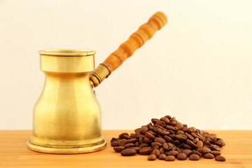 Old, vintage brass turkish coffee pot (dzhezve) with carved wooden handle and a pile of roasted coffee beans on a wooden table with a space for text