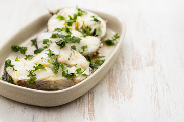 boiled perch with parsley and olive oil on dish on white wooden background