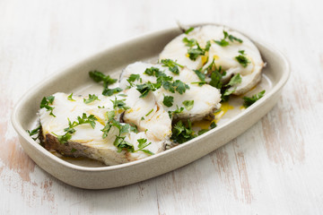 boiled perch with parsley and olive oil on dish on white wooden background