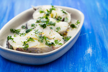 boiled perch with parsley and olive oil on dish on white wooden background