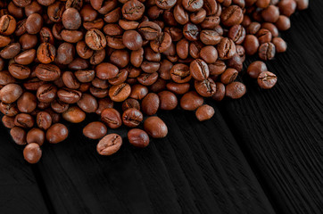 Roasted fragrant beans of black coffee are scattered on a black table