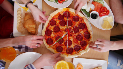Group of friends sitting in cafe. Taking pieces of pizza pepperoni