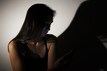 Teen girl excessively sitting at the phone at home. he is a victim of online social networks. Sad teen checking phone sitting on the floor in the living room at home with a dark background