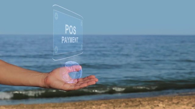 Male hands on the beach hold a conceptual hologram with the text POS Payment. A man with a holographic technology on the background of the sea
