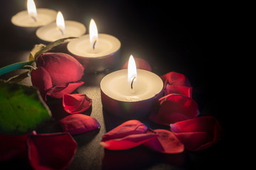 Fototapeta na wymiar Four tea candles and rose petals in the dark