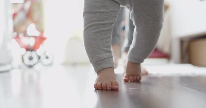 Mother assisting in her baby first steps in living room.