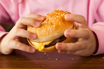 Little child eating a hamburger in the cafe