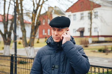 The man in the jacket and cap speaks on the phone.