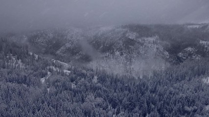 4K aerial flyover of mountains and forest during a snowstorm in the California Sierra Nevada Mountains.