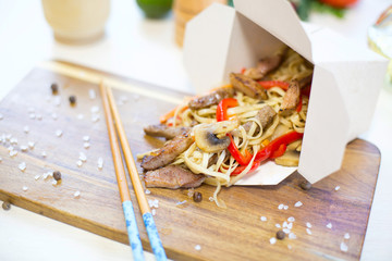 Noodles with pork and vegetables in take-out box on wooden table