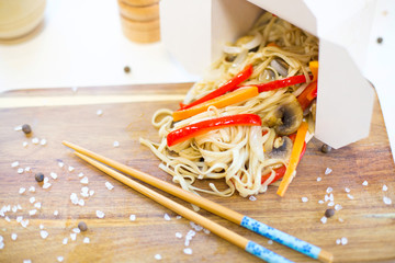 Noodles with pork and vegetables in take-out box on wooden table