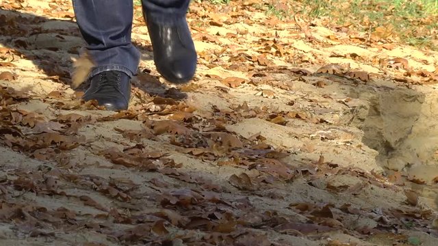man walks in black boots along the sandy beach. Dry leaves fly into the water.