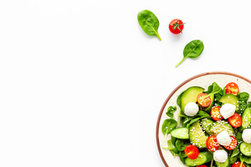 Fresh salad with mozzarella, spinach, cherry tomatoes, cucumber on plate on white background top...