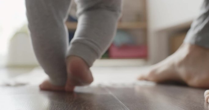 Mother assisting in her baby first steps in living room.