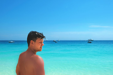 Young unshaven brunet man looks into the distance standing in Indian Ocean