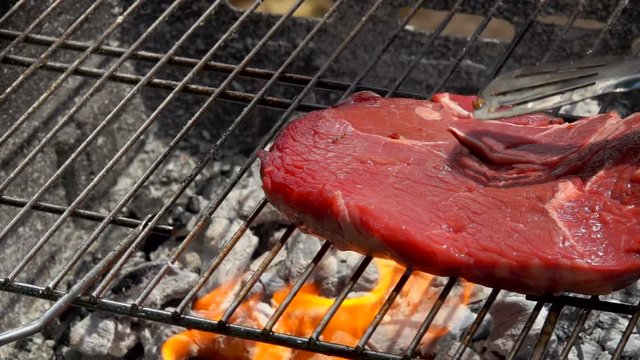 Hostess puts steak using metal tongs on the grill grate