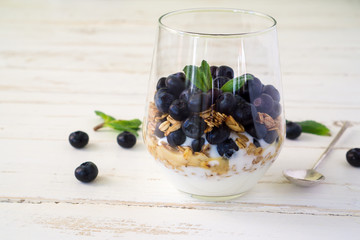 Oat granola with blueberries, yogurt and mint in a glass on a white and blue rustic background with copy space