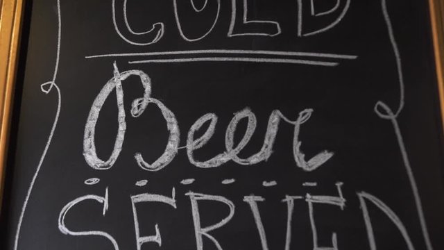 Craft cold beer served here insctiption by white chalk on black board. Invitation to brewery bar pub for drinking craft beer. Beer menu in bar pub.