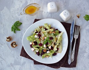 Green salad with boiled beetroot, feta and walnuts in a white plate on a gray concrete background. Seasoned with olive oil, grain mustard and vinegar. Healthy food. Top view.