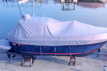 Boat covered with white tarpaulin in the seaport is parked on the pier.