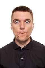 Obraz premium Handsome young man in a black shirt is making faces, while standing isolated on a white background