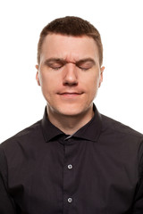 Handsome young man in a black shirt is making faces, while standing isolated on a white background