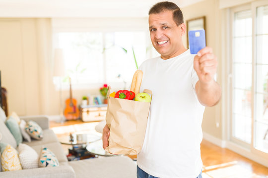 Middle age man holding groceries bag and showing credit card