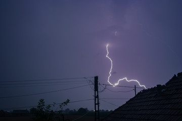 Lightning bolt strikes down to earth in a romanian village with power pole and power lines in the foreground