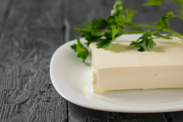 A rectangular piece of Serbian cheese in a white bowl on a wooden table. The view from the top. Dairy product.