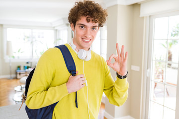 Fototapeta premium Young student man wearing headphones and backpack doing ok sign with fingers, excellent symbol