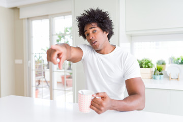 African American man with afro hair drinking a cup of coffee pointing with finger to the camera and to you, hand sign, positive and confident gesture from the front
