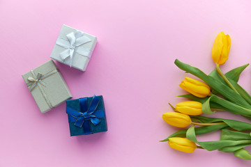 Yellow tulips and gift boxes on a pink background with copy space