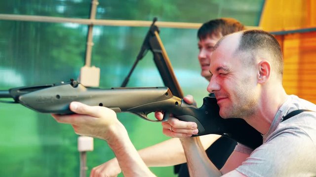 Close-up: Young guys shoot at shooting range from pneumatic guns, recharge cartridges