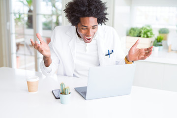 African American doctor man working with laptop at the clinic very happy and excited, winner expression celebrating victory screaming with big smile and raised hands