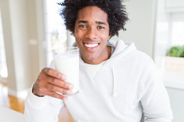African American man holding and drinking glass of milk with a happy face standing and smiling with...