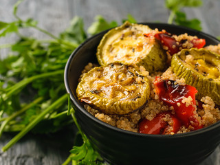Baked zucchini and bell pepper in a black bowl on a wooden table. Vegetarian dish. Natural plant food. The view from the top.