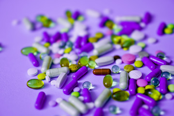 Spilled colored medications and pills on a purple background. Pharmacology and medicine struggle for health. Drug addiction. Treatment of various diseases